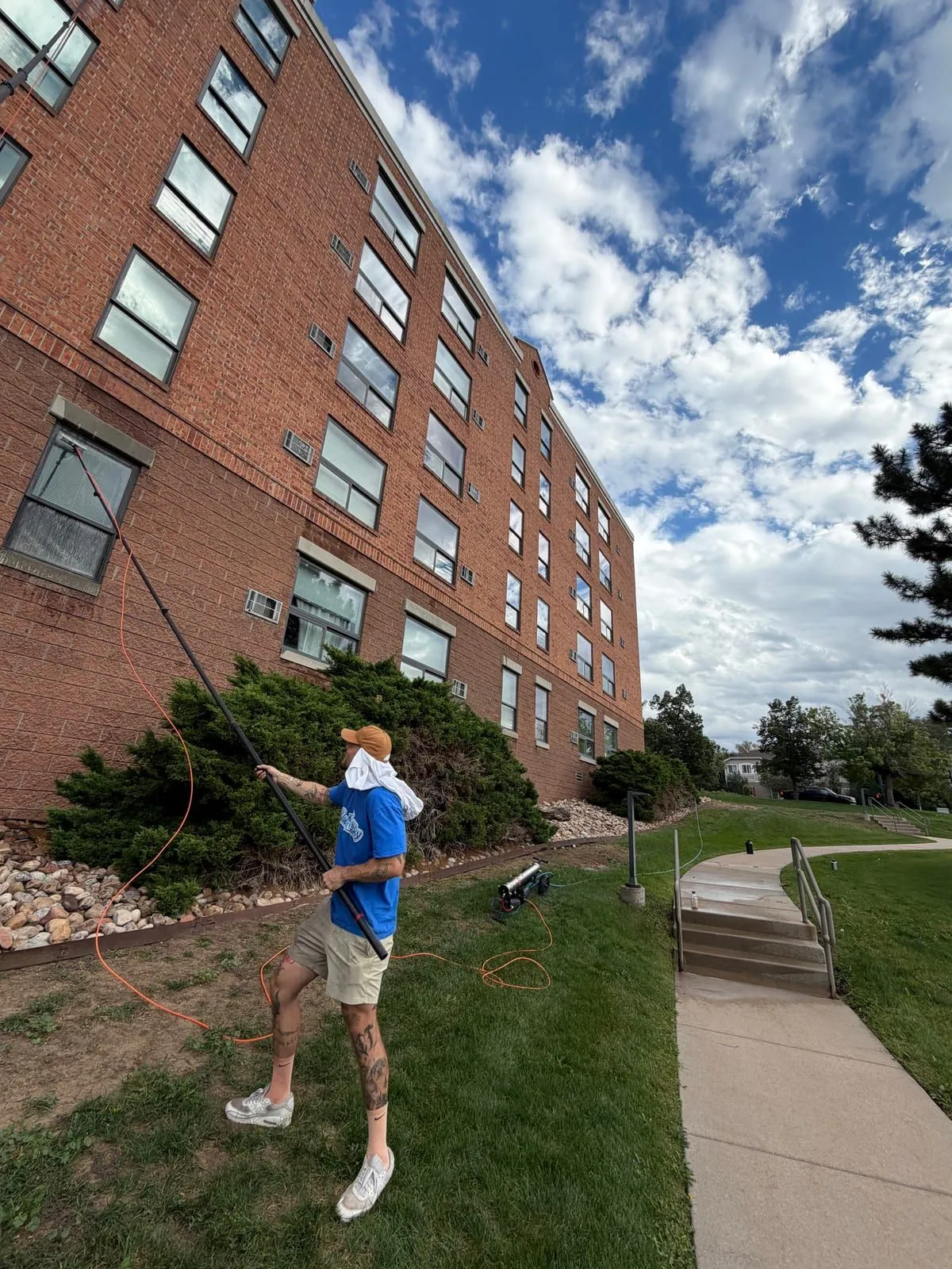 BlueSky technician using a water-fed pole to clean upper windows on a brick commercial building in Denver