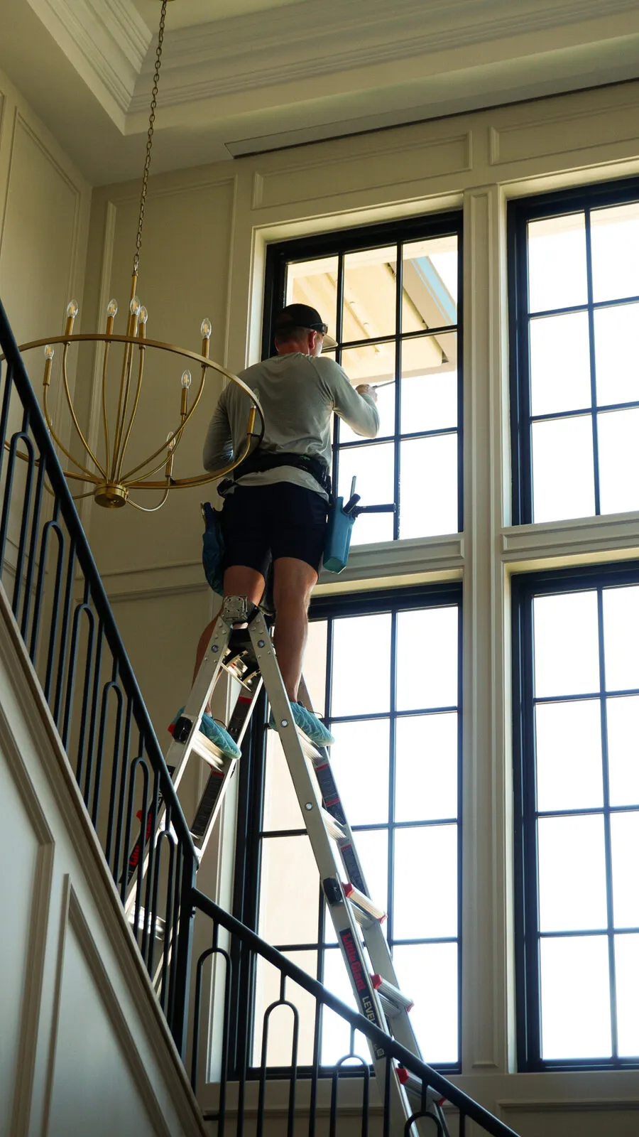 BlueSky technician on a ladder cleaning tall interior stairwell windows
