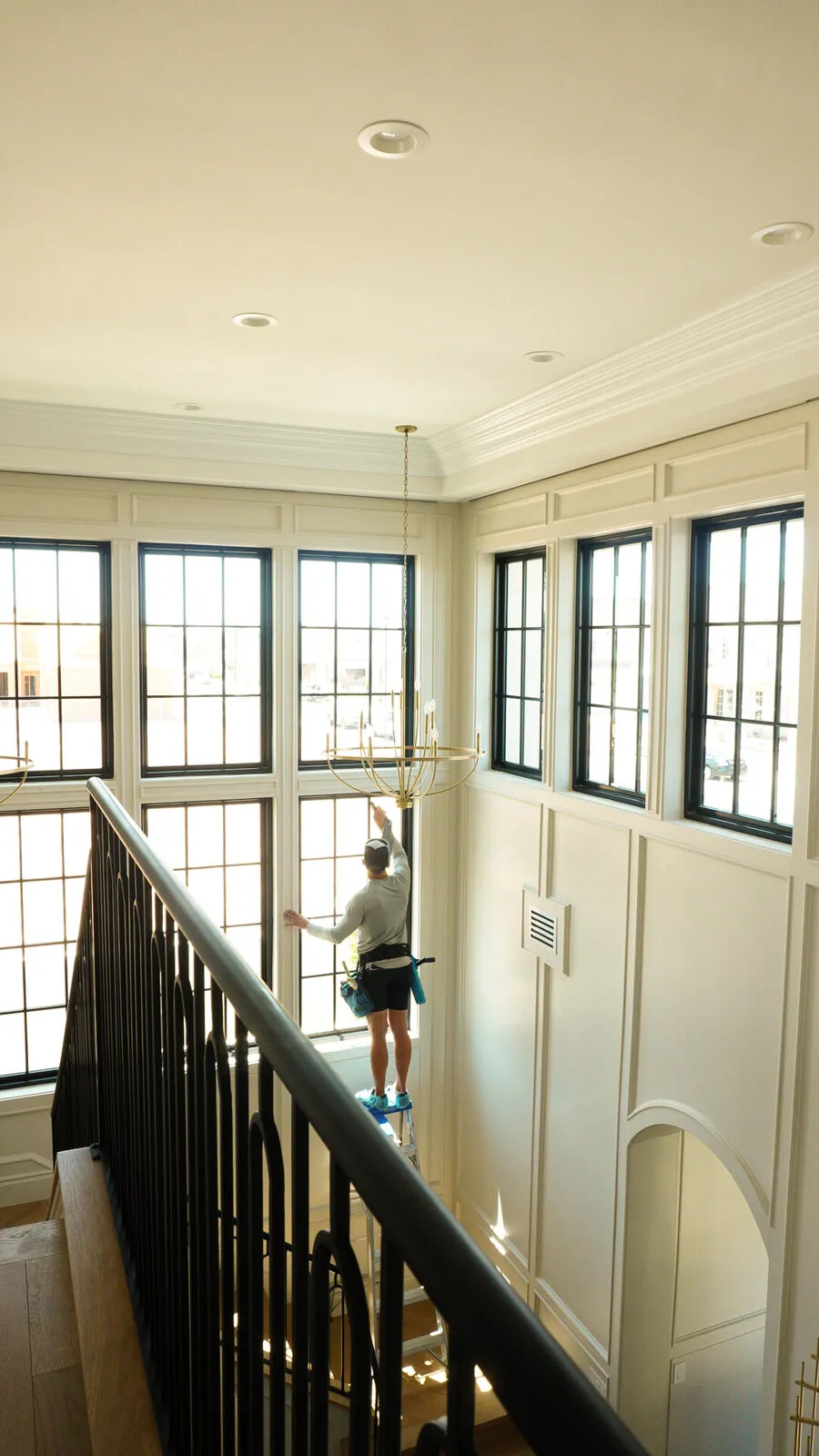 BlueSky technician cleaning two-story interior windows above a staircase