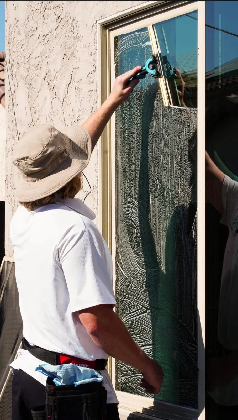 Close-up of a BlueSky technician working soap across a glass door with a squeegee