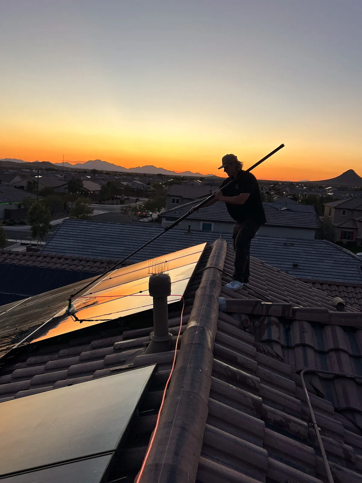BlueSky technician cleaning rooftop solar panels with a water-fed pole at sunset