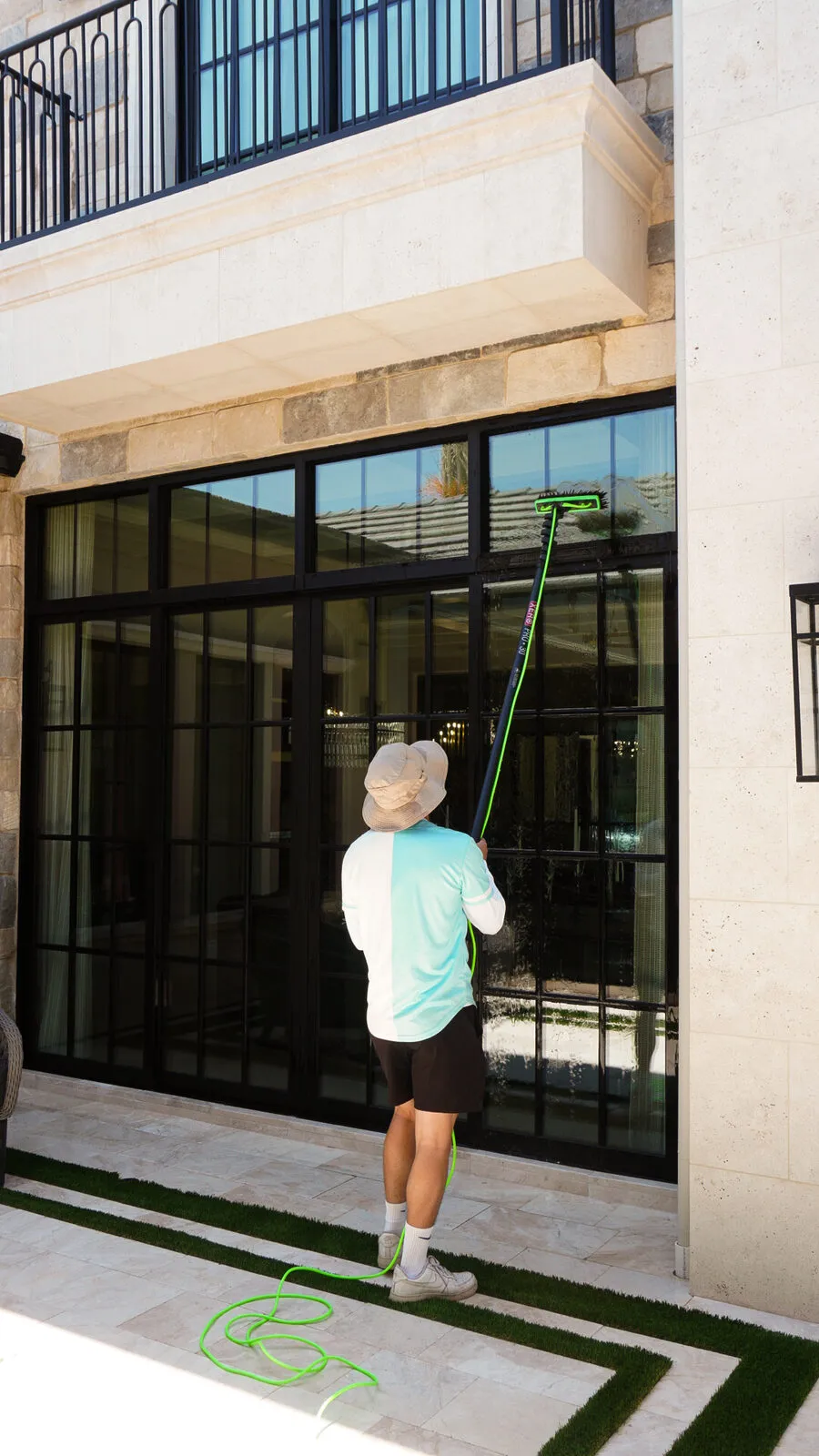 BlueSky technician cleaning tall exterior windows of a stone home with a water-fed pole
