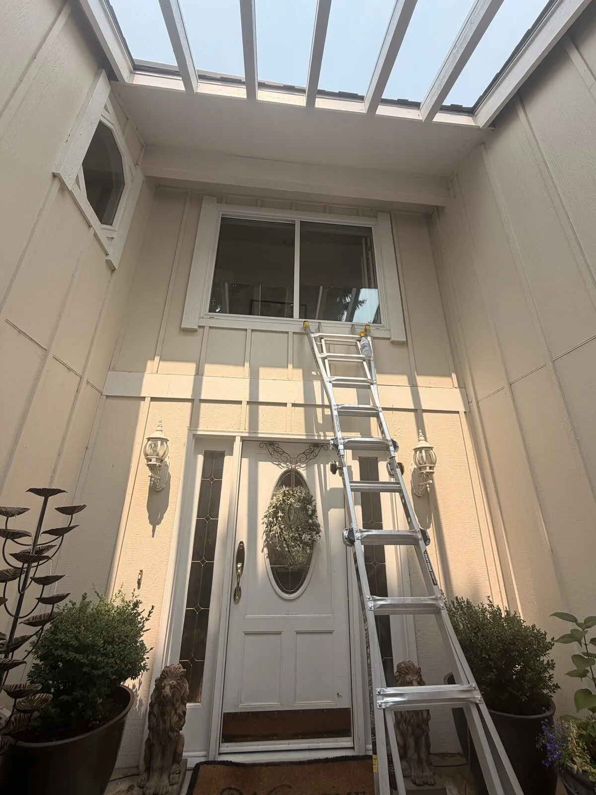 Ladder set up in a two-story skylighted entryway to clean the tall transom window above the front door of a Centennial, Colorado home