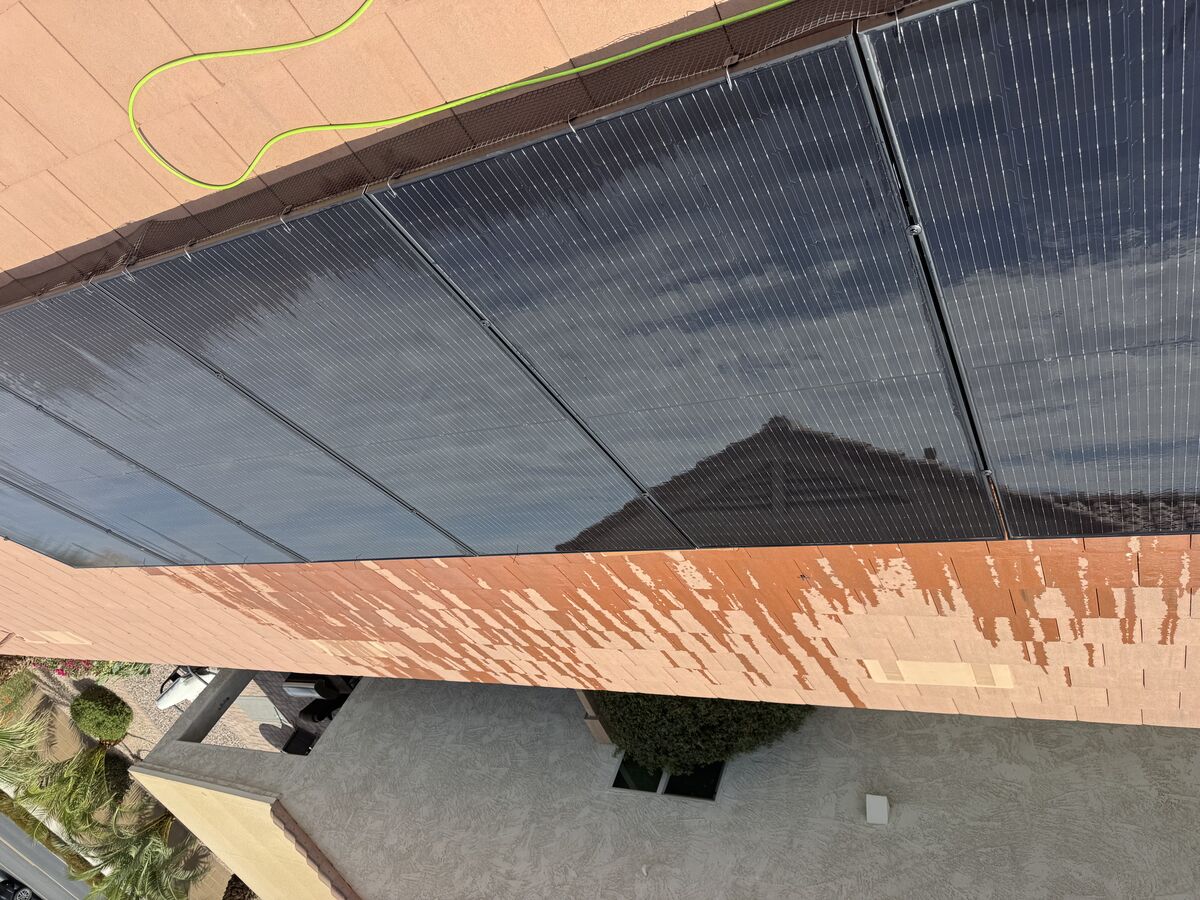 Rooftop solar array mid-cleaning, with cleaned panels visibly clearer than the uncleaned ones beside them